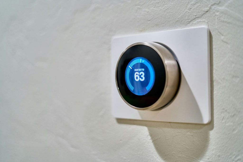 A round smart thermostat with a glowing digital display set at 63°F, mounted on a wall