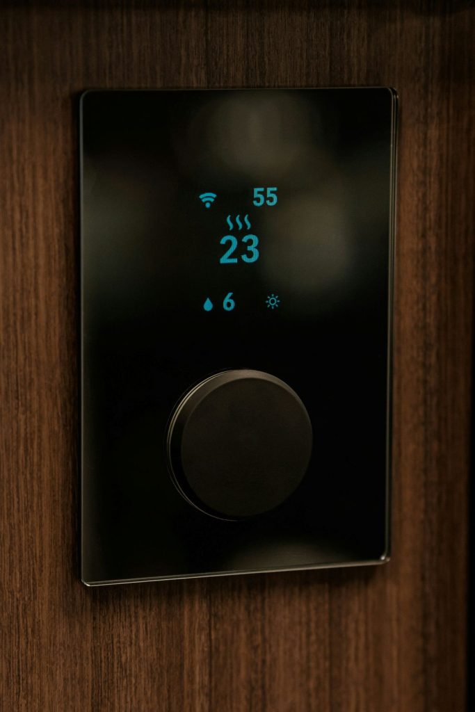 A sleek black digital thermostat with a circular control dial on a wooden wall