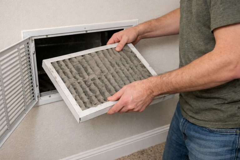 an illustrative image of a dusty air filter being removed from a wall grille by a resident