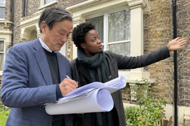 an illustrative image of two professional installers discussing heat pump installation plans outside a period property
