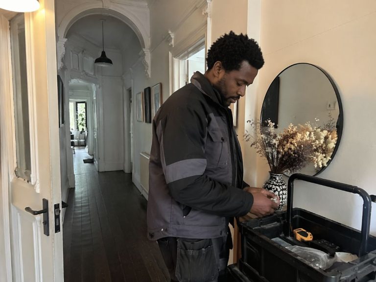 an illustrative image of an air conditioning engineer wearing smart work clothes preparing tools in the hallway of a London flat